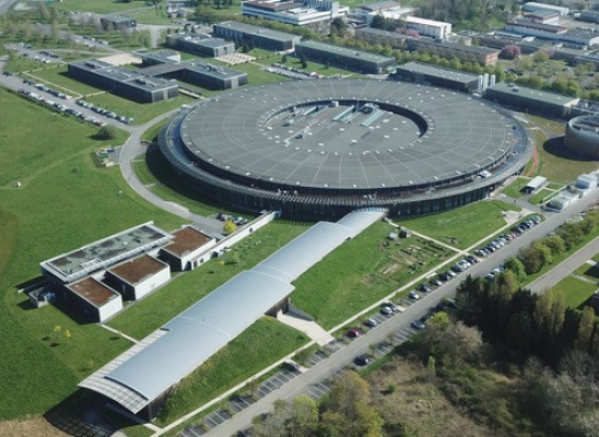Aerial view of SOLEIL synchrotron. Two elongated rectangular buildings emerge from a large circular building.